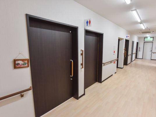 廊下にダークブラウンの木製のドアが並んでいる。壁だけでなく、ドアの開閉時に掴まるための縦型の手すりも設置されている。