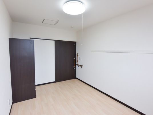 白色の壁と淡い色のフローリングの部屋で、黒っぽい色の木の引き戸があり、同じ色のクローゼットが置かれている。