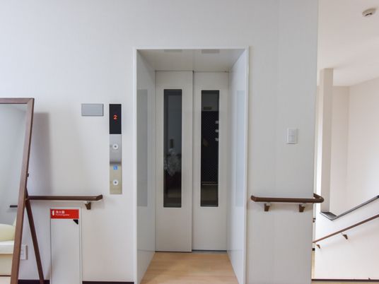 廊下にエレベーターと階段が並んでいる。エレベーターの近くには鏡があり、その向かいにソファが置かれている。