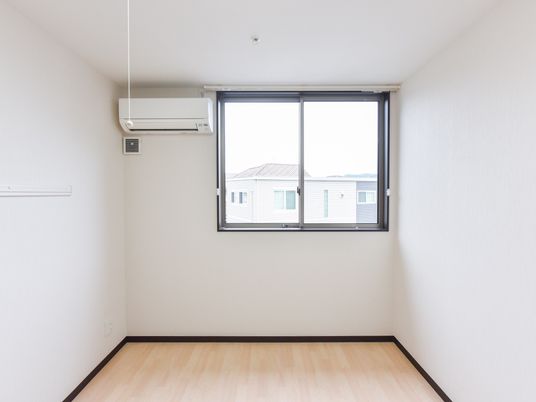 白を基調とした内装の居室である。壁にはエアコンとコンセントが設置されており、窓からは外の景色が良く見える。