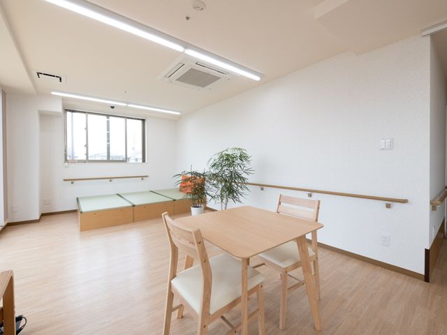 明るい居室の壁 共有スペース 自然光が差し込む清潔感のある居室で、リラックスして過ごせる環境が整っています。木の温もりを感じる家具が、穏やかな空間を創出しています。