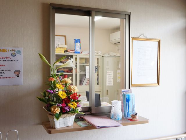 受付と花飾りの窓口 受付 明るく配されたフロントには、鮮やかな花が彩りを添え、来訪者を温かく迎えてくれる様子が伺えます。親しみやすい環境でのお仕事をご希望の方には適した空間です。