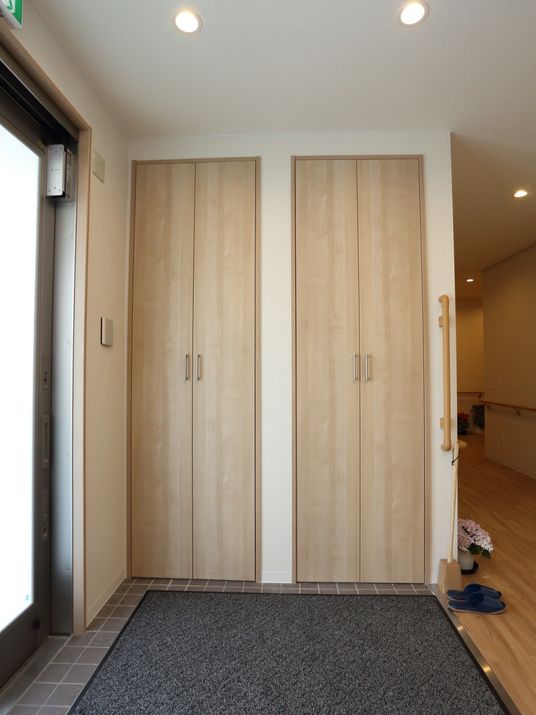 大きな観音扉のついた木目調の収納が２つある。その前には玄関マットが敷かれていて、スリッパが置かれている。