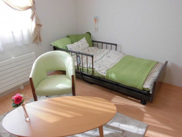 明るい居室のベッド 居室   自然光が差し込む、明るく落ち着いた居室です。ベッドとテーブルがあり、くつろぎやすい配置になっています。
