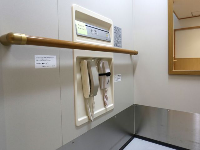 手すり付き廊下の角 エレベーター 手すりとコール装置が見える快適な通路です。これらの設備により、安全かつ円滑な移動が支援されています。