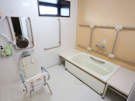 手すり付きの浴槽がある。壁にはさまざまな形の手すりが設置されている。床には入浴用の椅子が置かれ、前には洗面台や鏡がある。