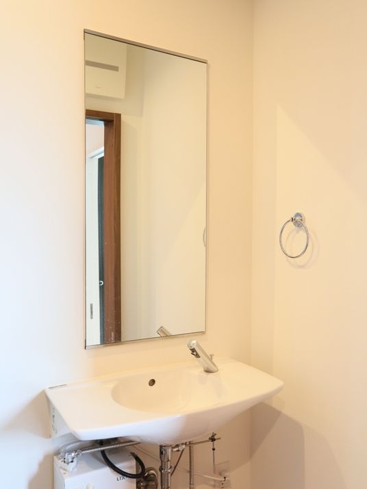 白色の洗面台があり、蛇口は自動感知センサー付きである。壁には、長方形の鏡とタオルハンガーが設置されている。