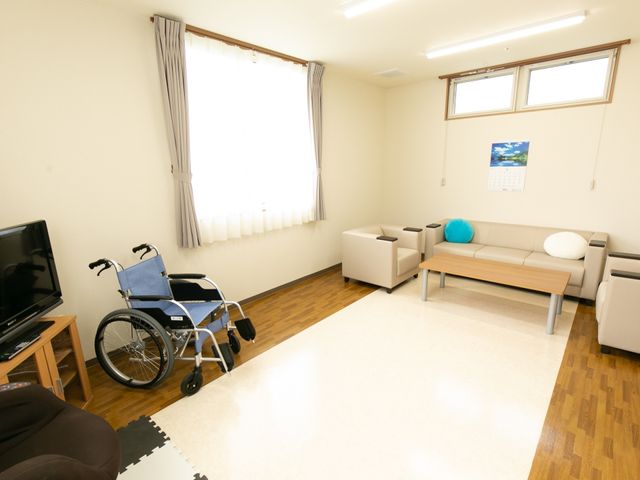 居心地のいい居室空間 共有スペース 落ち着いた色合いの居室では、ゆったりとしたソファや車椅子の配置が、日々の生活をイメージしやすくします。テレビも備え付けられ、快適な時間を過ごせるようになっています。
