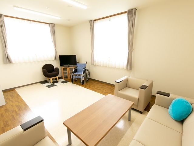 広々とした洋室の居室 共有スペース 開放的な居室は家具が整えられ、ゆったりとした時間を過ごすことができます。手すり付きの車椅子も備えており、安心してお過ごしいただけます。