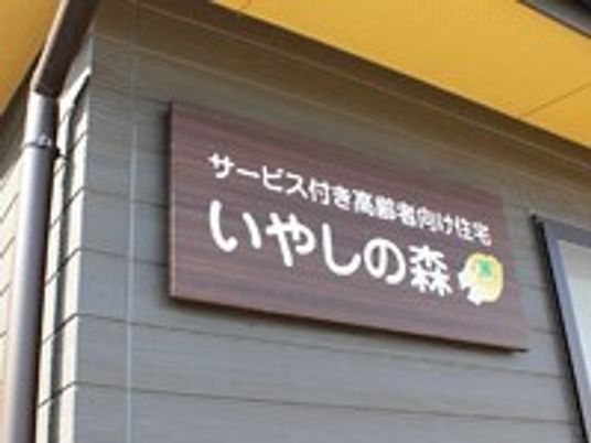 施設の写真 壁に施設名が書かれた看板が掛けられている。茶色の板に白く大きな字で書かれており、末尾に鳥の顔のようなマークがある。