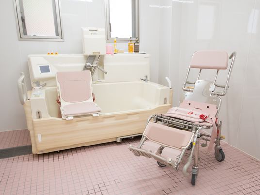 施設の写真 明るい浴室に浴槽と機械浴用の座椅子や浴用椅子が置かれている。介護が必要な入居者様も安心して入浴することができる。