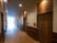 サムネイル 施設の写真 廊下は床や扉が木目調になっている。照明が扉の上にもついていて高級感がある。外からの陽の光も入り明るい。