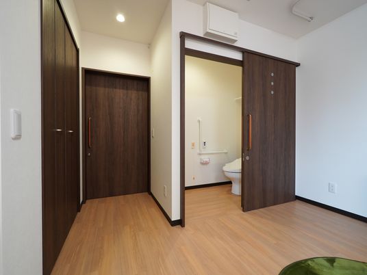 居室には折り畳み式の扉のクローゼットを設置している。ブラウン色で落ち着いた雰囲気である。白い壁で清潔感のある空間である。