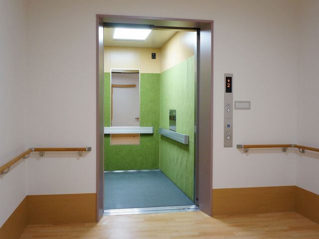 手すり付き廊下とエレベーター エレベーター 手すりが壁沿いに設置された廊下が見渡せます。自由に移動がしやすい環境が整っており、利用者の安全を配慮しています。