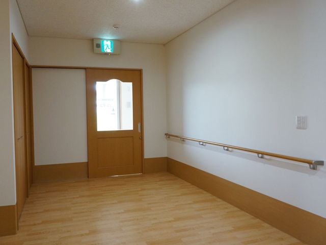 木目調の床と手すりの廊下 非常口 木目の温もりを感じる廊下には、壁に沿って手すりが設置されており、歩行時の安全を支えます。