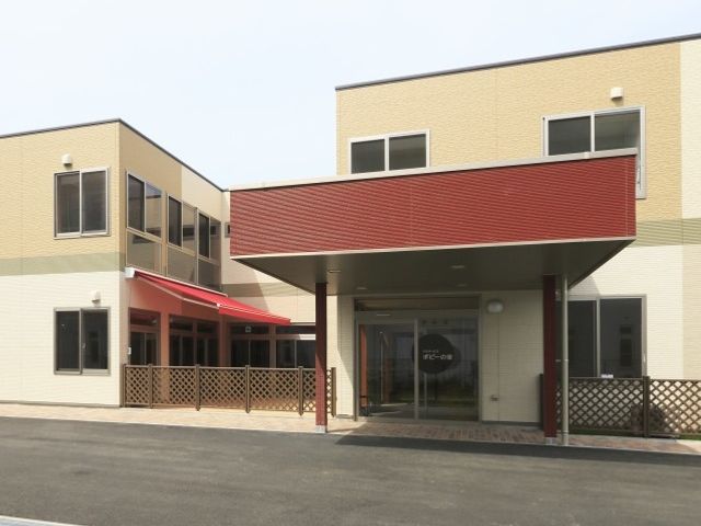 黄色い壁の明るい建物エントランス 外観 広々とした駐車場に面したエントランスは、訪れる方々を暖かく迎えてくれます。明るく開放感あるデザインで、皆様の出勤にも安心感を与える空間です。