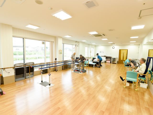 リハビリ中の人々と設備 機能訓練室 広々とした訓練室で、専門のスタッフが入居者のリハビリをサポートしています。それぞれのニーズに合わせた設備が整っており、安心して身体機能の向上を目指せます。