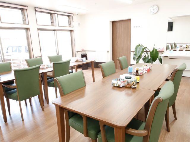 明るいダイニング空間 談話室 木のテーブルと緑の椅子が並ぶ温かみのある食堂です。共に食事を楽しむコミュニケーションの場となっています。