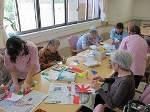 活動する人々の多目的室 共有スペース ゆとりある空間で、入居者が手工芸などの活動に没頭しています。スタッフも笑顔でサポートする姿から、あたたかい雰囲気が伝わってきます。