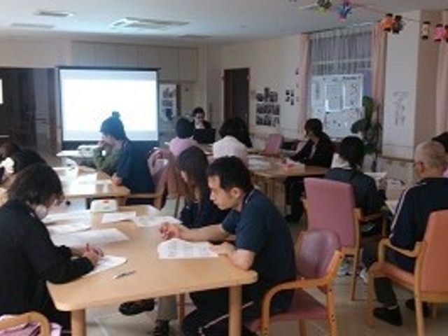集い身を寛ぐ多目的室 スタッフ 広々とした多目的室には、皆が集い交流する様子が見受けられ、和やかな時間を過ごしているようです。各自がテーブルに向かい、集中して何かをしている姿が印象的です。