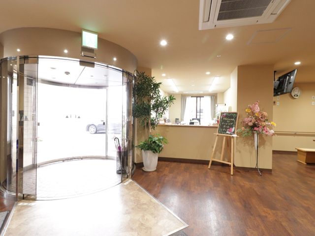 エントランスの様子 玄関 歓迎の花と掲示板が迎える明るく開放的なエントランスです。手すりや床の転倒防止設計に配慮された空間で、ここから新たな職場生活が始まります。