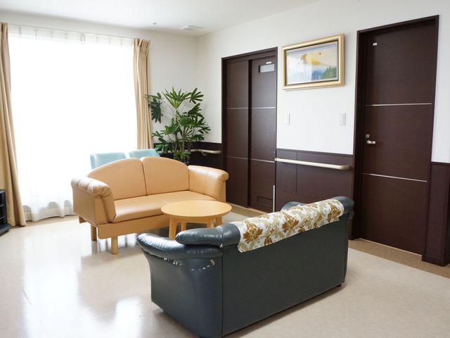 居心地の良い居室の一角 談話コーナー ゆったりとした座り心地のソファが配置され、明るい窓辺で憩いの時を過ごすことができます。落ち着いた色合いの壁と調和する家具が、温かみのある空間を演出しています。