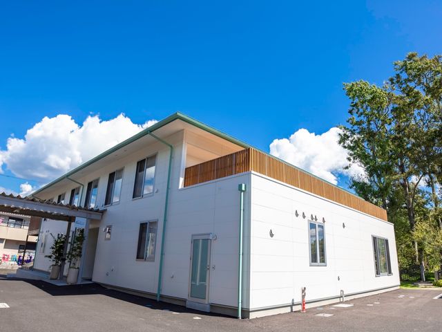 清潔な外観の建物 車寄せ 爽やかな青空のもと、清潔感あふれる白い壁の建物が光を反射しています。緑に囲まれ、快適な職場環境を提供している様子が伺えます。