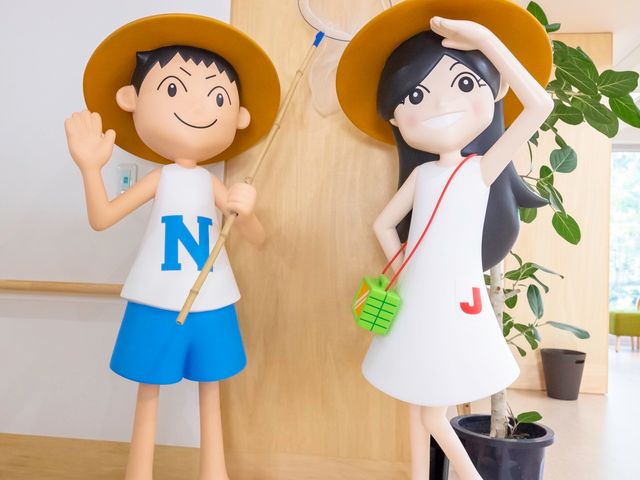 キャラクター像と観葉植物 マスコット 笑顔を浮かべたキャラクターの像が、来場者へ温かい歓迎の気持ちを伝えています。ロビーには緑も配置され、明るい雰囲気になっています。