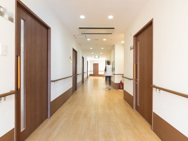 清潔感のある廊下 通路 床は木目調で温かみがあり、手すりも完備していて安全に配慮された廊下です。職員の方が積極的に動いていて、活気が感じられます。