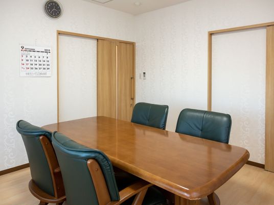 四人掛けの大きなテーブルと革張りのクッションの利いた椅子が置かれている部屋。スライド式の扉があり、カレンダーと時計が掛けられている。
