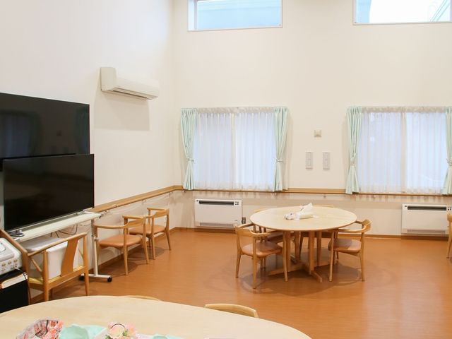 広々とした共有リビング ダイニング 天井が高く、明るい日差しが差し込む共有リビングです。円卓が置かれ、憩いの時間を過ごすための落ち着いた雰囲気が演出されています。
