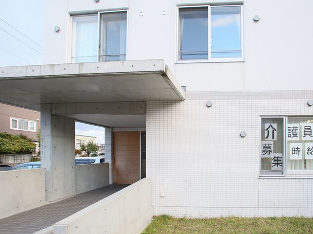 白い壁の建物エントランス 外観 広々としたエントランスがお迎えする安全で機能的な建物です。来訪者の皆様が快適に出入りできるように設計されています。