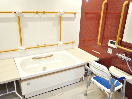 白い浴槽と蛇口が設置されている。壁には頑丈な手すりがつけられ、背もたれとひじ掛け付きのシャワーチェアが置かれている。