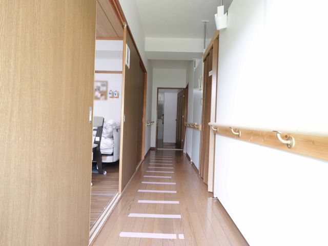 清潔な廊下と部屋の一部 廊下 手すりが設けられた廊下は、清潔感があり明るく、安心して歩行できる環境が整っています。部屋の入口からは、快適な居住空間の一端をうかがうことができます。