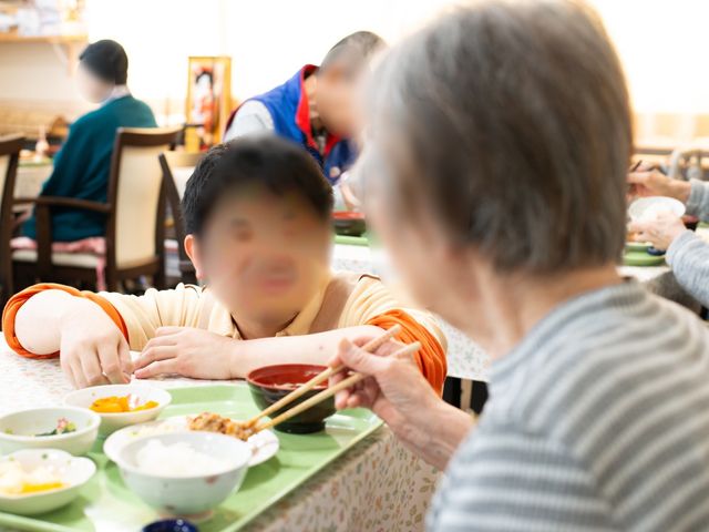 共有食事スペース 笑顔 明るい食堂で楽しむ食事の時。多様な料理を前にして、利用者同士が和やかな会話を交わしています。