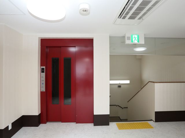赤いエレベーターと階段 エレベーター 利便性を重視した設計で、赤いエレベーターが目を引く廊下です。緊急時の避難経路も整備されており、安心して勤務できます。