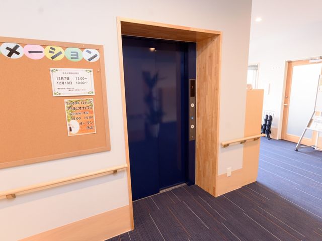木目調のエレベーター入口 エレベーター 広々とした廊下の先にあるエレベーターは、バリアフリー設計が施されており、ご高齢の方々の安全な移動をサポートしています。