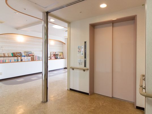 施設の写真 エレベーターが１基設置されており、目の前の壁には手すりが備えつけられている。奥の棚には本がたくさん並べられている。