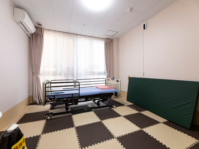 整った清潔な居室 居室 広々とした空間の居室で、窓からの自然光がゆったりとした時間を演出しています。機能的なベッドと床のクッションマットが心地よい環境を提供します。