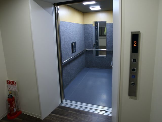 モダンなエレベーター入口 廊下 ゆったりとした空間のエレベーターは、車椅子の方も快適に移動できるよう配慮されています。手すりと床の視認性を高めた設計で、安心してご利用いただけます。