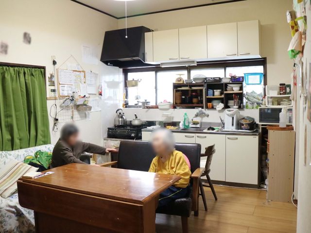 共有リビングの一コマ キッチン 家庭的な雰囲気のリビングで、入居者の方々がくつろいでいる様子が伺えます。暖かな光とともに、日常のひとときを過ごされています。