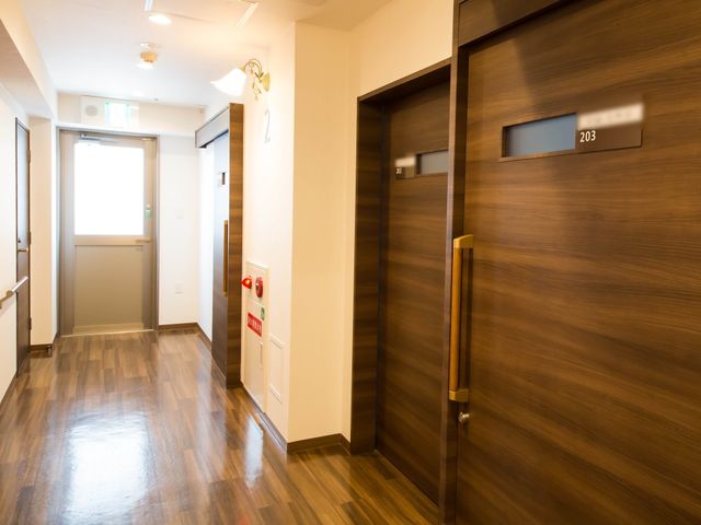 廊下の綺麗な居室扉 共用廊下 暖かい雰囲気の明るい廊下です。安らぎと落ち着きを提供し、スタッフの方々が快適に過ごせる環境が整っています。