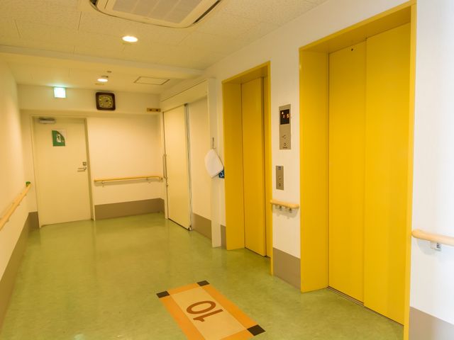 明るい廊下とエレベーター エレベーターホール 手すり付きの廊下はゆったりとした設計で、誰もが安心して移動できる造りになっています。エレベーターも隣接しバリアフリーへの配慮がみられます。