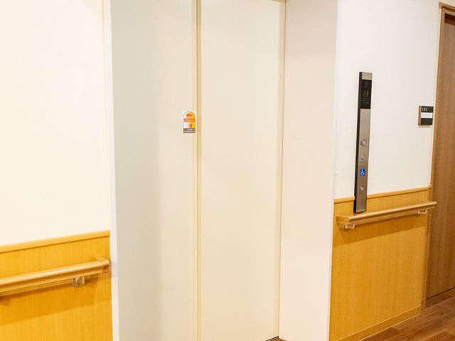 床材が木目調のエレベーター エレベーター 木目調の床材が温かみを感じさせるエレベーター前です。手すりもついており、安心して移動できます。