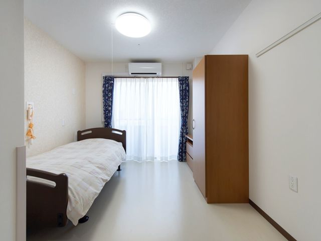 清潔な個室の居室 居室 ゆったりとしたベッドと明るいカーテンが印象的な個室では、静かなひとときをお過ごしいただけます。十分な収納スペースも配慮されています。