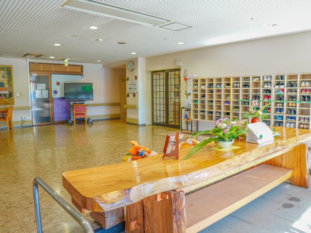 明るい空間のロビー エントランス 天然木のテーブルが設置された広々とした休憩スペースです。清潔感のある環境で読書や交流をお楽しみいただけます。