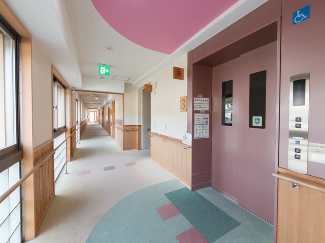 廊下とエレベーターの風景 エレベーター ゆとりある幅広の廊下が、明るく開放感のある環境を提供しています。車椅子利用者も安心して移動できる設計です。