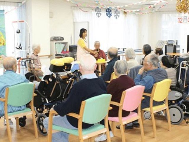 椅子に座る利用者とスタッフ レクリエーション ゆったりとした多目的室で、利用者同士が穏やかなひとときを過ごしています。明るく開放的なこの空間で、スタッフとの様々な活動が行えます。