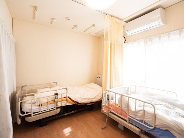 共同の居室空間 寝室 床にはフローリングが施され、日差しの降り注ぐ明るい居室で、利用者の方々が落ち着いて生活できる設計です。