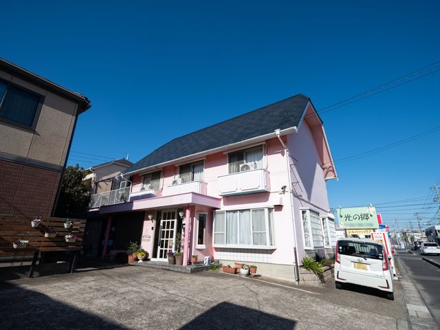 ピンクの外観の建物 外観 明るいピンク色が心温まる建物の入口です。周りには植物も配置され、訪れる人を穏やかに迎えます。
